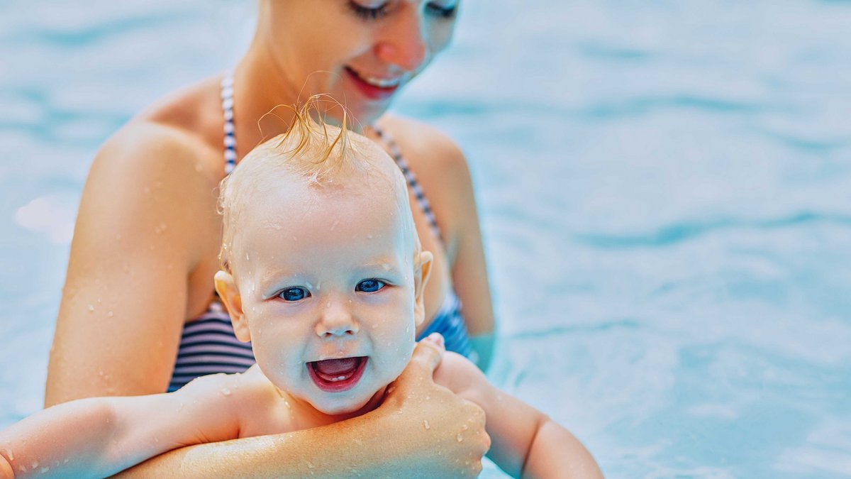 Eine Frau steht im Wasser und hält einen Arm um ein Kind das vor ihr steht.