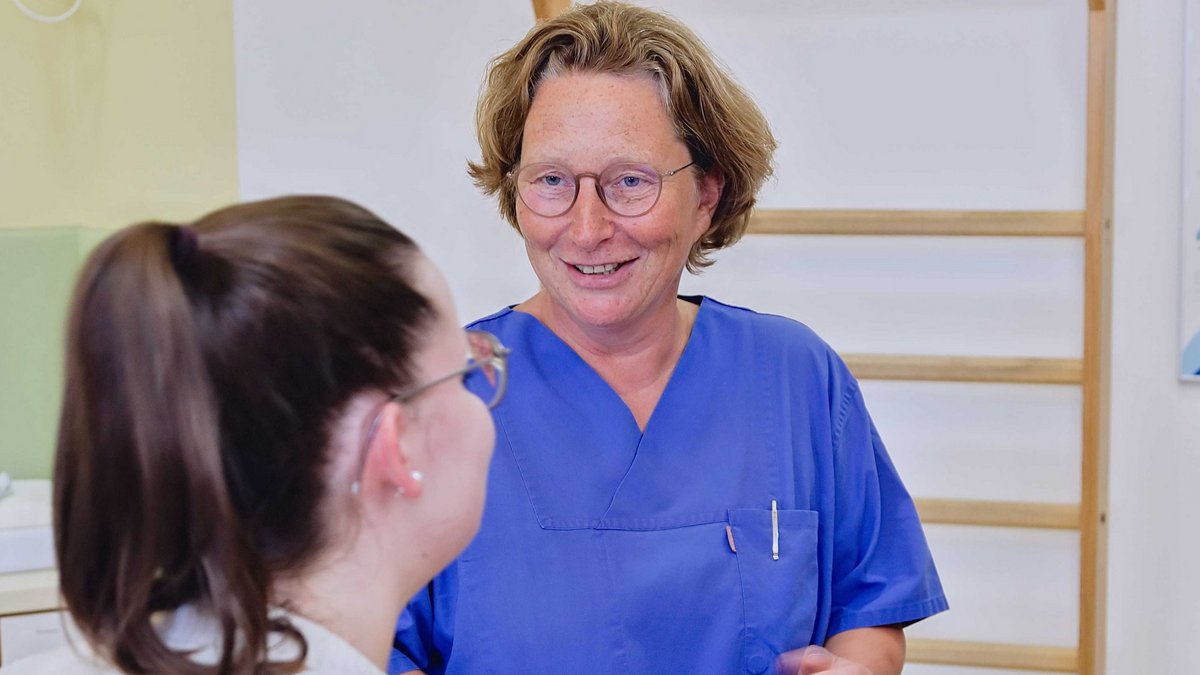 Eine Dame mit Brille und blauem T-Shirt spricht zu einer etwas jüngeren Dame mit Brille und Pferdeschwanz.
